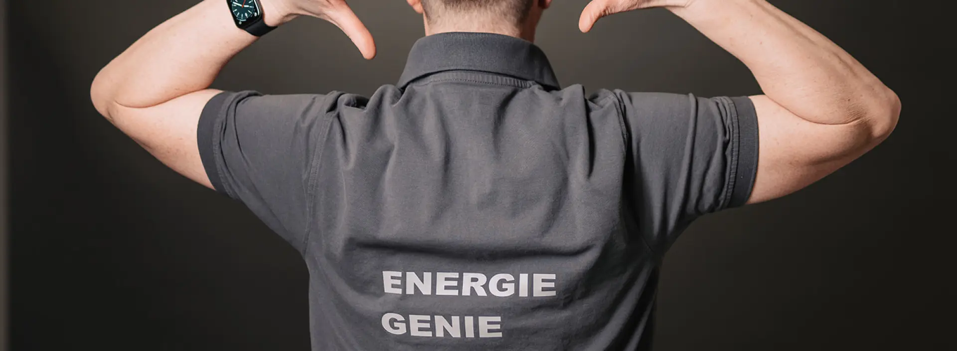 Mann zeigt stolz auf sein 'Energie Genie' Polo-Shirt, symbolisiert Expertise in Energieeffizienz.